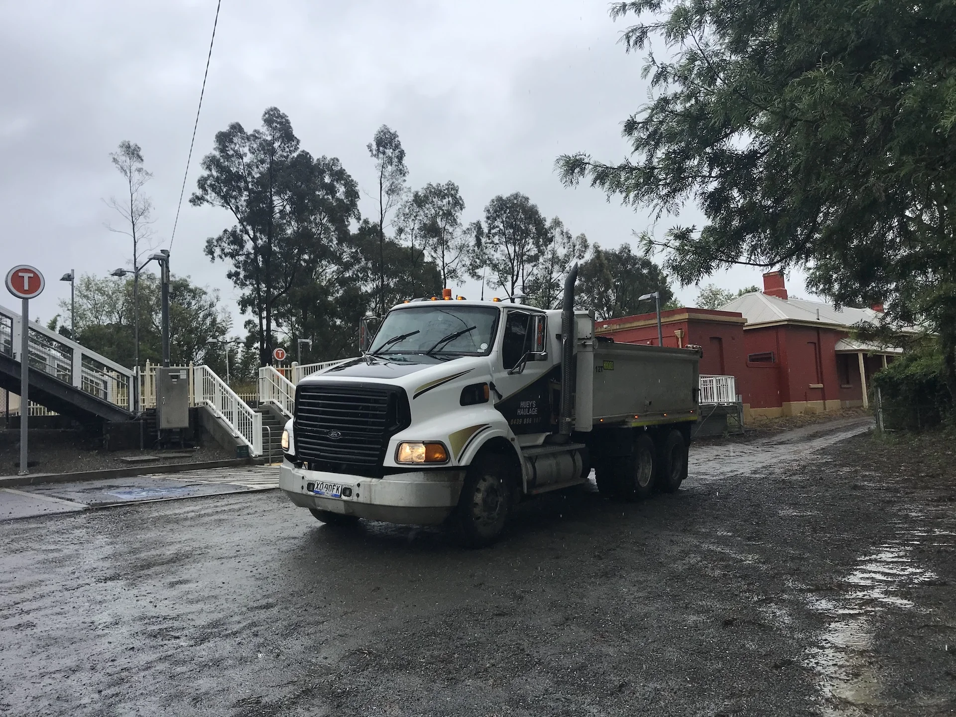 Huey's Haulage tipper truck on a wet civil works site beside a level crossing