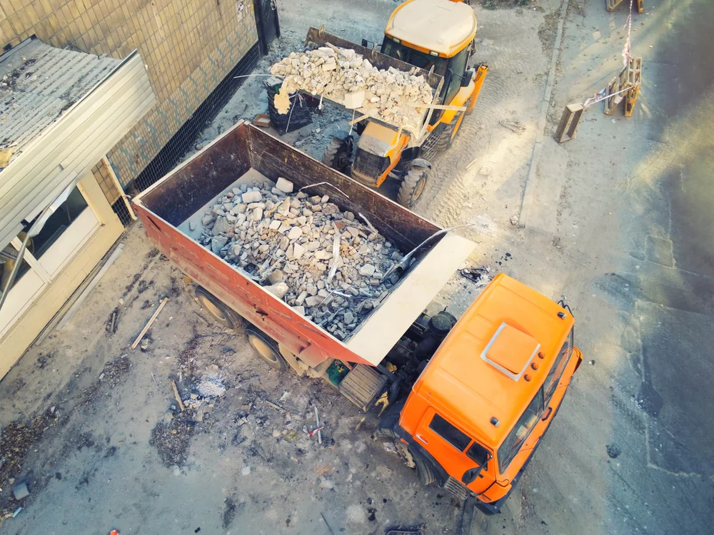 Aerial view of a tipper truck and loader clearing concrete rubble from a demolition site