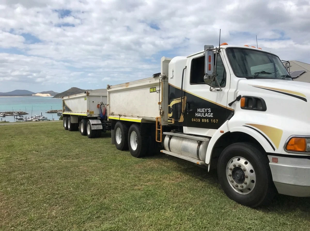 Huey's Haulage truck and dog trailer parked on grass beside Port Stephens water