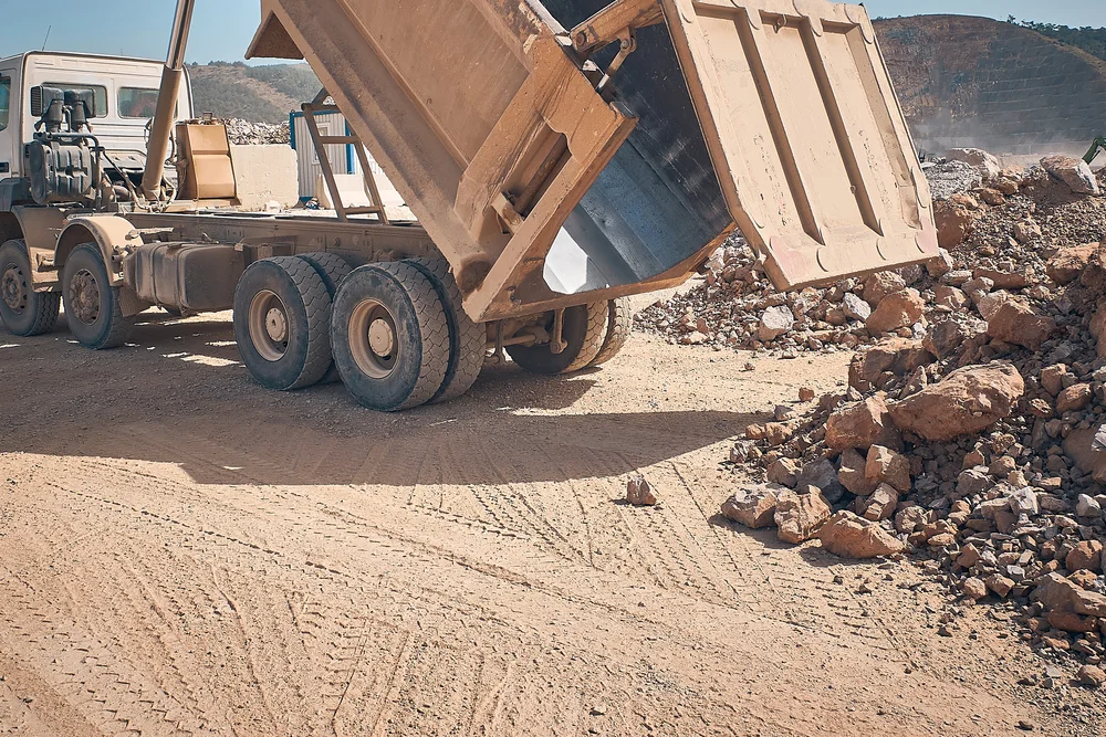 Tipper truck tipping rock into a stockpile on a dusty quarry floor