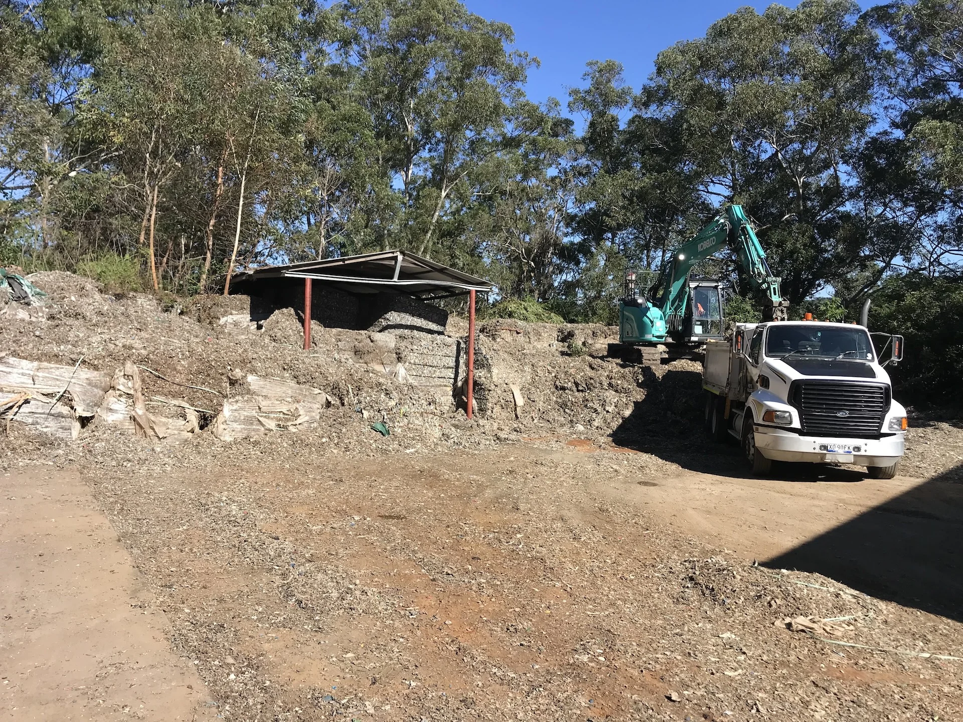Excavator and Huey's Haulage tipper truck working a cut site surrounded by bushland